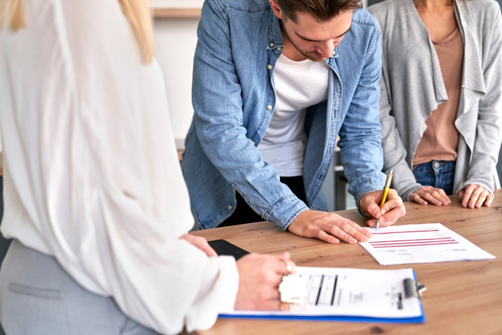 Young caucasian couple signing house purchase agreement with a real estate agent